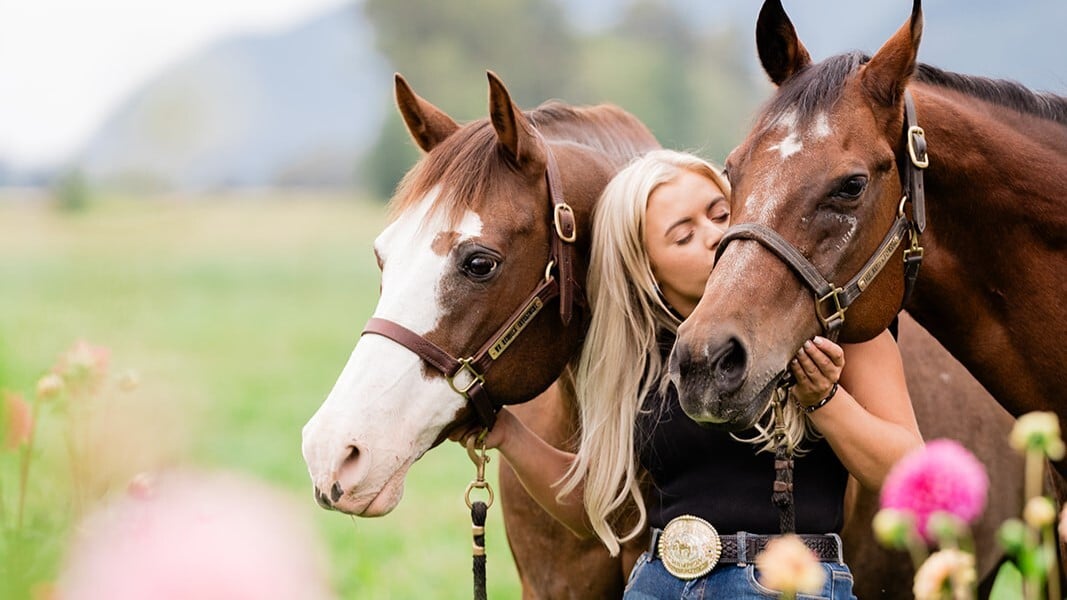 A woman with two horses in a field with flowers.